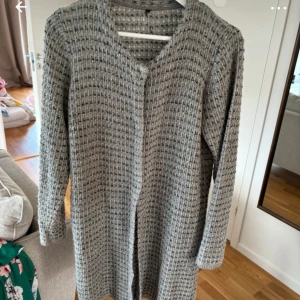 Grå stickad kofta - Säljer en mysig grå stickad kofta med lång ärm och ett enkelt mönster. Perfekt för kyliga dagar och lätt att matcha med olika outfits. Koftan har en öppen design utan knappar eller dragkedja.