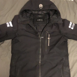 Svart jacka från Sail Racing - Säljer en svart jacka från Sail Racing med huva och dragkedja. Jackan är vattentät, vindtät och andas, med tejpade sömmar och DWR-beläggning. Perfekt för blåsiga och regniga dagar. Skick 9/10 