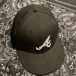Svart keps från New Era - Säljer en svart keps från New Era, modell 59FIFTY. Kepsen har en broderad vit logga på framsidan och är i mycket bra skick. Perfekt för både vardag och sportiga aktiviteter. Passar de flesta stilar och är ett måste för kepsälskare!