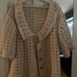 Beige stickad kofta med knappar - Mysig beige stickad kofta med stora knappar framtill. Den har en luftig design med trekvartsärmar och en bred krage. Perfekt för en avslappnad stil hemma eller en sval sommarkväll. 🧶✨