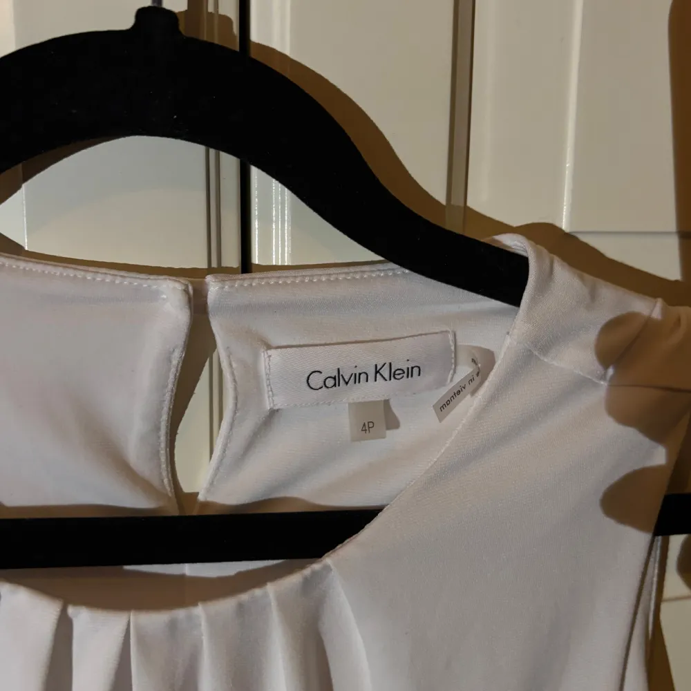 Säljer en stilren vit ärmlös topp från Calvin Klein i mycket bra skick. Toppen har en elegant rynkad detalj vid halsen och är perfekt för både vardag och fest. Materialet känns mjukt och bekvämt mot huden. Passar perfekt till sommarens alla tillfällen!. Toppar.