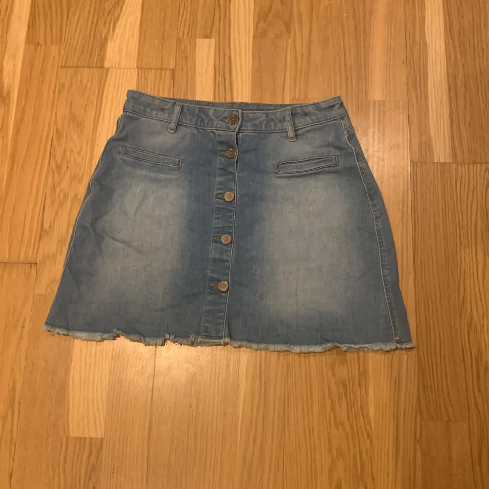 Säljer en snygg jeanskjol från Lindex i storlek EUR 170. Kjolen har en klassisk blå denimfärg med knappar framtill och en fransig nederkant för en cool look. Perfekt för både vardag och festliga tillfällen. 🦋(liten fläck med av svart bläck). Kjolar.