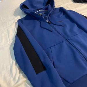Blå hoodie från Hugo Boss - Blå BOSS zip up hoodie från deras senaste kollektion, köpta på Hennings ganska nyligen så skicket är felfritt. Pris går alltid diskutera vid snabb affär 
