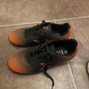 Svarta och orange fotbollsskor - Säljer ett par coola fotbollsskor från Joma i svart och orange. Skorna har ett snyggt mönster och snörning för bra passform. Perfekta för spel på konstgräs med sina greppvänliga sulor. Använda men i bra skick!