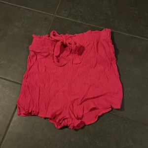 Rosa shorts från Divided - Säljer ett par supergulliga rosa shorts från Divided i storlek S. De är högmidjade med en söt knytning i midjan och har en skön, lös passform. Perfekta för sommardagar eller en avslappnad vårlook. Materialet är lätt och luftigt, vilket gör dem idealiska för varma dagar. 🩷