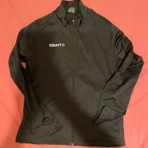Svart träningsjacka från Craft - Säljer en svart träningsjacka från Craft i mycket bra skick. Jackan har en dragkedja framtill och är långärmad, perfekt för löpning eller annan träning. Den är gjord i ett lätt och bekvämt material som andas bra. Passar perfekt för höst och vårträning! Passar både killar och tjejer, priser går alltid att diskutera🤩Passar Dam i storlek M med