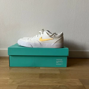 Vita Nike sneakers med gul detalj - Säljer ett par fräscha vita Nike sneakers med en snygg gul swoosh. Charge SLR - Nike SB