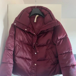 Vinröd pufferjacka från Hugo Boss - Säljer en snygg vinröd pufferjacka från Hugo Boss. Jackan är perfekt för kalla dagar med sin vadderade design och har en hög krage för extra värme. Jackan är köpt förra vintern och använd en vinter. Alla bilder är egna förutom sista! 