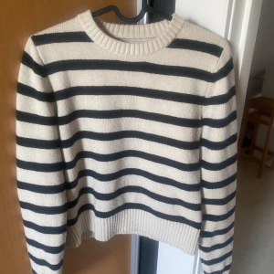 Randig stickad tröja - Säljer en superfin randig tröja i beige och svart med en klassisk rund halsringning. Perfekt för höst och vinter. Den är lite croppad vilket är perfekt för att ha ett fint linne under
