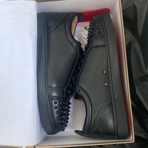 Svarta sneakers med nitar - Säljer ett par Louboutins. De har en klassisk röd sula och snörning framtill. Skorna är i mycket bra skick och kommer i originalkartong.