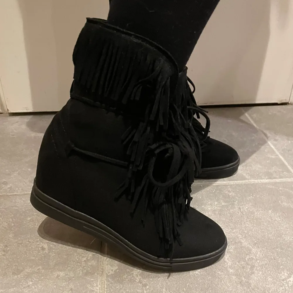 Säljer ett par svarta boots i syntetmaterial med coola fransdetaljer. De har en bekväm passform och är perfekta för höst och vinter. Skorna har en diskret klack och är i mycket bra skick. Storlek 37, skriv om du har frågor!. Skor.