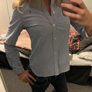 Blå skjorta från Ralph Lauren - Säljer en klassisk blå skjorta från Ralph Lauren i storlek 16. Skjortan har en stilren design med knappar och det ikoniska broderade logotypen på bröstet. Perfekt för både vardag och fest! 💙