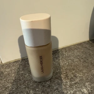 Laura Mercier Real Flawless Foundation - Säljer en Laura Mercier Real Flawless Foundation i en elegant glasflaska med vit kork. Denna foundation ger en viktlös och perfekt finish, perfekt för en naturlig look. Flaskan är stilren och lätt att använda. Shade:2N1 Cashew