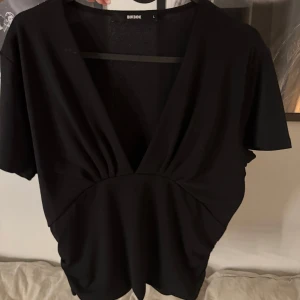 Svart v-ringad topp från Bik Bok - Säljer en stilren svart topp från Bik Bok i storlek L. Den har en djup v-ringning och korta ärmar, perfekt för både vardag och fest. Materialet känns mjukt och bekvämt mot huden. 