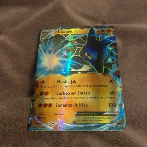 Lucario Pokémon-kort - Det här är ett holografiskt Lucario Pokémon-kort med 180 HP. Kortet har attacker som Missile Jab, Corkscrew Smash och Somersault Kick. Det är ett Pokémon-EX kort, vilket betyder att det är extra kraftfullt och sällsynt. Perfekt för samlare eller för att stärka din kortlek i strid!