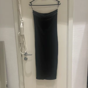 Svart axelbandslös klänning - Snygg svart axelbandslös klänning i ett elegant och stilrent snitt. Perfekt för festliga tillfällen eller en utekväll. Klänningen har en tight passform som framhäver figuren och är i ett mjukt och bekvämt material.