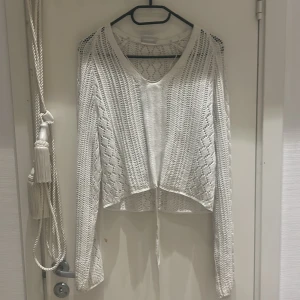 Vit stickad tröja med knyt - Säljer en superfin vit stickad tröja med v-ringning och knyt framtill. Den är perfekt för vår och sommar, med en luftig och bekväm passform. Tröjan har långa ärmar och en lätt croppad stil som ger en avslappnad look. Perfekt att matcha med jeans eller kjol!