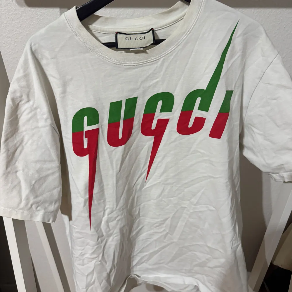 Säljer en snygg vit t-shirt från Gucci i storlek XL. Den har ett coolt tryck i grönt och rött på framsidan. Perfekt för sommaren eller våren. T-shirten är i bra skick och gjord av mjuk bomull. Passar perfekt till både vardag och fest!. T-shirts.