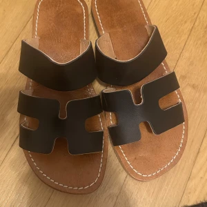 Bruna sandaler i skinn - Säljer ett par snygga bruna sandaler i äkta skinn med en stilren design. De har en bred rem över foten och en bekväm sula med bra grepp. Perfekta för sommardagar och avslappnade tillfällen. Använda men i bra skick.