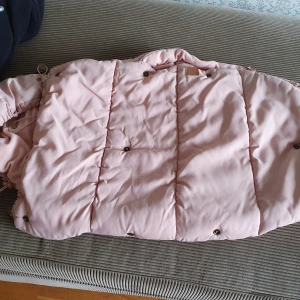 Rosa och svart åkpåse från BabyBjörn - Säljer en mysig rosa och svart åkpåse från BabyBjörn. Perfekt för att hålla ditt barn varmt under kalla dagar. Åkpåsen har en quiltad design och är tillverkad i mjukt material. Den har praktiska knappar för enkel användning. Passar perfekt för höst och vinter.