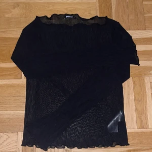 Svart ribbad topp från Gina Tricot - Super snygg svart ribbad topp från Gina Tricot i transparent material. Den har långa ärmar och en vågig kant vid halsen och ärmsluten. Tyvärr är storleken för stor för mig och därför har den inte kommit till användning.💗💗💗skriv för fler bilder!