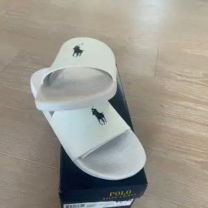 Säljer ett par nya oanvända vita sandaler från Polo Ralph Lauren. Str 42. De har en stilren design med det klassiska Polo-loggan i svart på ovansidan. (Nypris 475, mitt pris 200kr). Hör gärna av dig vid frågor!