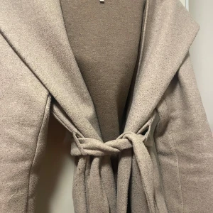 Beige kappa med knytband - Säljer en superfin beige kappa i ull med knytband i midjan. Perfekt för höst och vår! Den har en elegant och stilren design med långa ärmar och en mjuk känsla. Passar både till vardags och festliga tillfällen. 🧥✨
