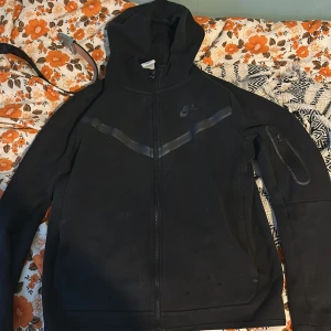Svart hoodie från Nike - Säljer en svart hoodie från Nike i bra skick. Den har en dragkedja framtill och en liten ficka med dragkedja på ärmen. Perfekt för höst och vår, och den är långärmad. Passar både för träning och vardag.