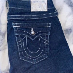 Mörkblå jeans från True Religion - Säljer ett par snygga mörkblå jeans från True Religion i storlek 28. De har coola vita sömmar och pärldetaljer på fickorna. Perfekta för både vardag eller när du vill va lite extra snygg! Dom är använda typ 4 gånger, inga tecken på användning (som nya) PRIS GÅR ATT DISKUTERA ❤️