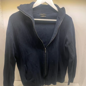 Mörkblå zip tröja från Massimo Dutti - Säljer en snygg och stilren mörkblå hoodie från Massimo Dutti. Den har en dragkedja framtill och är tillverkad i ett mjukt material som känns skönt mot huden. Perfekt för både höst och vinter. Passar lika bra till vardags som till en avslappnad kväll med vänner.