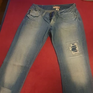 Blå jeans med slitningar - Säljer ett par blå jeans i bra skick med coola slitningar på ena benet. De har en klassisk femficksdesign och är perfekta för en avslappnad stil. Passar bra till både vardag och fest. Sköna och trendiga!