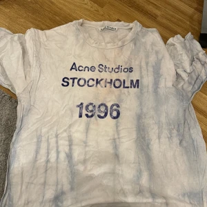 T-shirt från Acne Studios - Säljer en t-shirt från Acne Studios med tryck 'STOCKHOLM 1996' i blått. Blå och rosa pasteller. T-shirten har en avslappnad passform och är kortärmad. Perfekt för en casual look eller sommarens äventyr. Lite sliten men fortfarande snygg! Köpt för 2000kr mitt pris 600kr