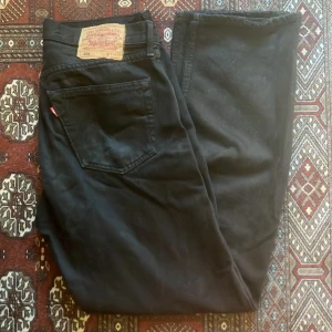 Svarta Levis 501 jeans - Säljer ett par klassiska svarta Levis 501 jeans i bra skick. De har en rak passform och är tillverkade i slitstarkt denim. Köpta i USA, skulle gissa tidigt 2000-tusen tal.