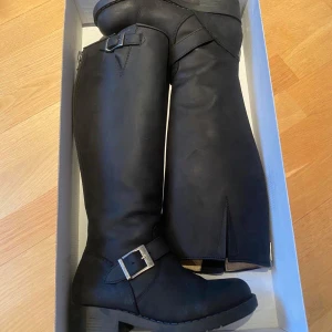 Svarta stövlar med spänne - Snygga svarta stövlar i äkta läder med dragkedja och spänne. Perfekta för höst och vinter med en robust klack och slitstark sula. De har en stilren design med en dekorativ rem och metallspänne vid ankeln. Priset kan diskuteras!