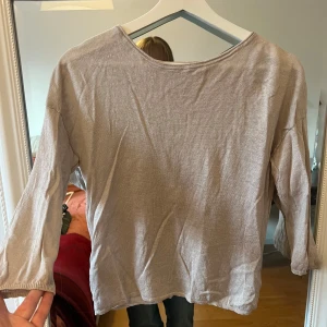 Beige tröja med omlott-design - Säljer en snygg beige tröja med omlott-design på baksidan. Den har trekvartsärmar och är perfekt för både vår och höst. Materialet känns mjukt och bekvämt, vilket gör den idealisk för vardagsbruk. Passar bra till jeans eller kjol för en avslappnad look.