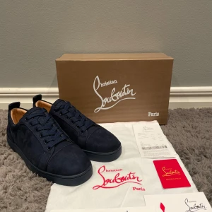 Mörkblå sneakers från Christian Louboutin - Säljer ett par snygga mörkblå sneakers från Christian Louboutin i nytt skick. Skorna är i mocka med klassisk röd sula och har snörning. Perfekta för både vardag och fest! Kommer med originalkartong och dustbag.