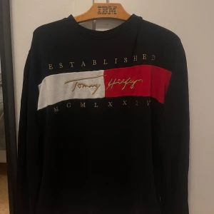  tröja från Tommy Hilfiger - Säljer en snygg  tröja från Tommy Hilfiger med deras ikoniska logga i rött och vitt på bröstet. Tröjan har långa ärmar och är perfekt för en casual look. Passar både till vardags och fest. Skön och stilren design! Nypris 1000 mitt pris 200
