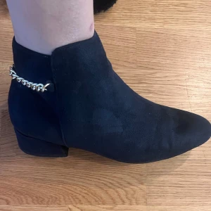 Svarta boots med kedjedetalj - Snygga marinblåa boots i mocka med en cool kedjedetalj runt hälen. De har en dragkedja på sidan för enkel på- och avtagning. Perfekta för höst och vinter, och ger en stilren touch till vilken outfit som helst. Passar både till vardags och fest!