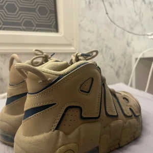 Beige Nike sneakers - Säljer ett par coola beige Nike sneakers med blå detaljer. Skorna har en chunky sula och tydlig 'AIR' text på sidan. De är i bra skick och perfekta för vardagsbruk. Storleken är US 3.5Y, vilket motsvarar ungefär dam 36. Använt 1 gång