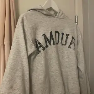 Säljer en supermjuk och bekväm grå hoodie med texten 'AMOUR' i svart på framsidan. Perfekt för mysiga dagar eller en avslappnad stil. Den har en klassisk passform med långa ärmar och en praktisk huva. Passar perfekt till jeans eller leggings! STL 140 men passar mig som bär xs, s