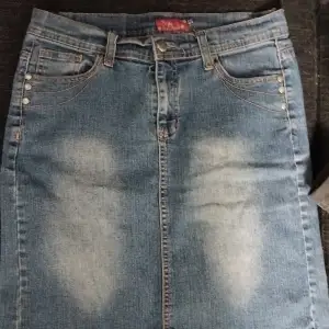 Säljer en snygg jeanskjol i klassisk blå denim med coola slitningar framtill. Kjolen har en rak passform och knappar i midjan. Perfekt för en avslappnad vardagslook eller en utekväll med vänner. Passar bra till både sneakers och klackar!