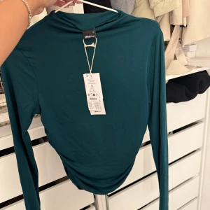 Grön långärmad topp från Gina Tricot -  Långärmad tröja från ginatricot med prislappen kvar!  Toppen har rynkningar i sidorna. Den har figurnära passform och utsvängd ärm.