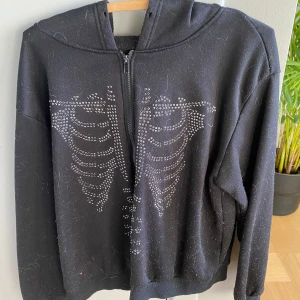Svart hoodie med skelettmönster - Cool svart hoodie med dragkedja och huva. Den har ett unikt skelettmönster i silverfärgade nitar på framsidan. Perfekt för höst och vinter. Tröjan är i bra skick men har lite ludd som enkelt kan tas bort. Tvättas innan jag postas!💖