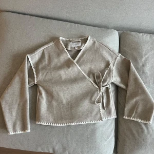 Beige omlottopp från VILA - Tröja med vita detaljer. Crossover modell, med knyte. Den är lite tjockare i materialet. Helt oanvänd.