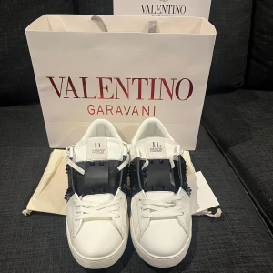 Valentino Garavani sneakers - Säljer ett par snygga Valentino Garavani sneakers i vitt skinn med svarta detaljer. Skorna har coola spikar på sidorna och klassisk snörning. De är i bra skick och kommer med originalpåse och förpackning. Perfekta för både vardag och fest! Den har dock en spike som har gått av men syns verkligen inte eftersom att det är på insidan. Andvänt cirka 3 gånger men har gjort i ordning dom som nya. Med mera frågor hör av er och pris går att diskutera!🙌🤝