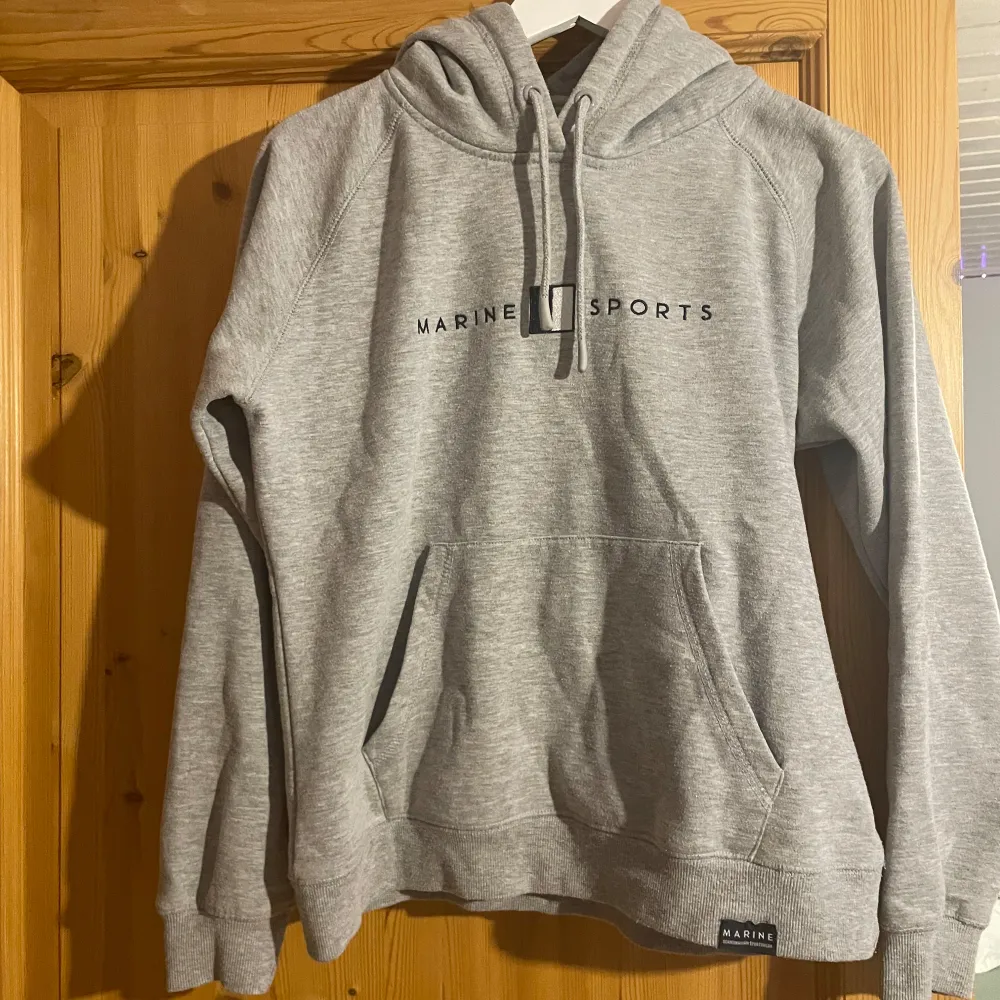 Säljer en grå hoodie från Marine Sports i storlek M. Den är supermjuk och perfekt för kalla dagar. Hoodien har en känguruficka och justerbar dragsko i huvan. Perfekt för både vardag och träning!. Hoodies.