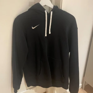 Svart hoodie från Nike - Säljer en stilren svart hoodie från Nike i bra skick. Den har en klassisk design med vit logga på bröstet och justerbar dragsko i huvan. Perfekt för både träning och vardag. Superbekväm och passar till allt! 🖤