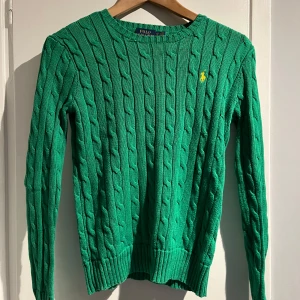 Grön kabelstickad tröja från Ralph Lauren - Grön Ralph Lauren kanelstickad tröja med gul logga. Fint skick. Storlek XS. 