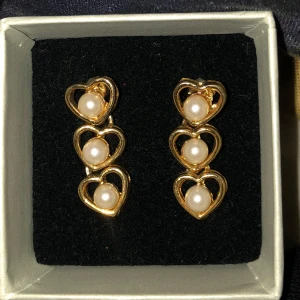 guldörhängen med hjärtan och pärlor - säljer ett par guldörhängen med tre hjärtan i rad, varje hjärta har en vit pärla i mitten. det är i jättefint skick.💞