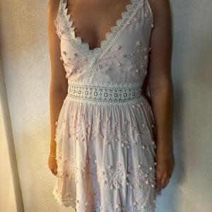 By Malina klänning - Säljer denna galet fina ljusrosa klänning från By Malina. Den har broderade blommor och en söt spetskant i midjan. Klänningen är ärmlös och har en kort längd som ger en luftig känsla.